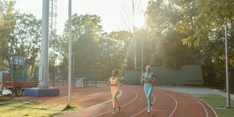 Two women jogging on an outdoor track, enjoying exercise and fitness in the morning sun.