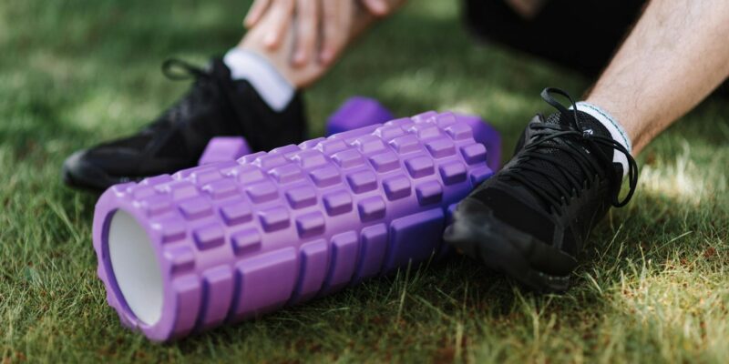 Black sneakers and purple foam roller on grass, outdoor fitness scene.