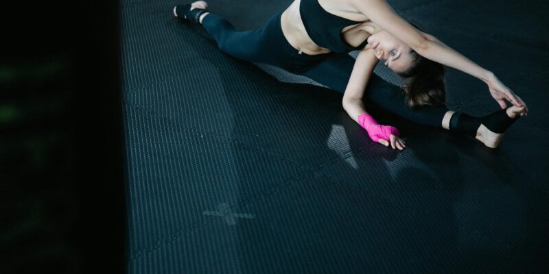 A woman performs a stretching exercise on a gym mat, showcasing flexibility.
