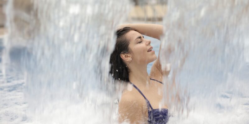 A woman relaxing under a waterfall in a summer outdoor pool, enjoying leisure time.