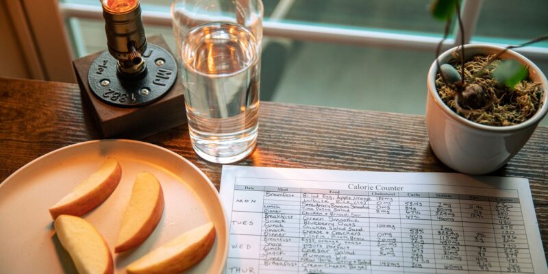 A cozy desk setup with apple slices, calorie counter, and water glass in warm lighting.
