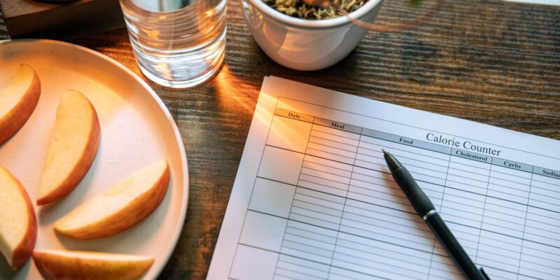 Calorie counting setup with apple slices and glass of water on a wooden table.