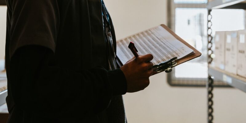 Industrial worker managing inventory in a warehouse with a clipboard and checklist.
