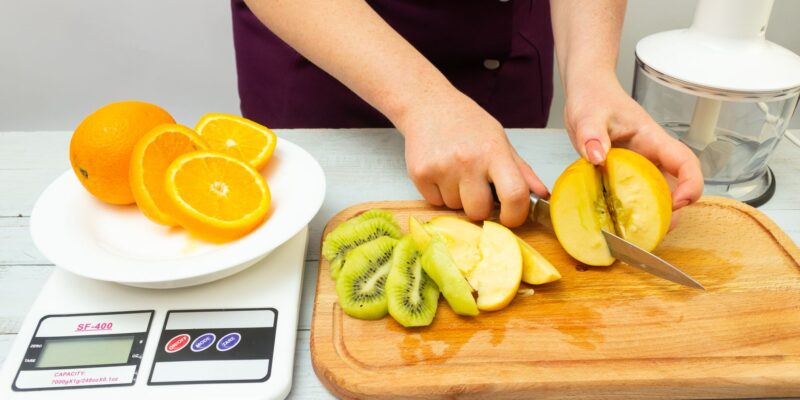 Woman slicing fruits including apple, kiwi, and orange for a healthy meal preparation.